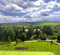 View from a 2-room apartment in the West of Tvrdošín, with a playground and hilly landscape.