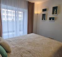 Bedroom in a two-room apartment with a bed, pillows, and decorative shelves on the wall.