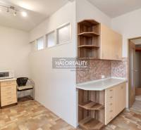 A kitchen in a 3-room apartment with a microwave, a chair, and cabinets for storage.