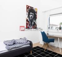 A simple room with a table, a chair, a bed, and a colorful painting on the wall in a three-room apartment.