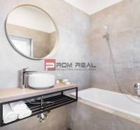 A bathroom with a sink, bathtub, and round mirror in a 3-room apartment.