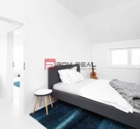 A bedroom with a bed, a blue carpet, and a coat rack in a three-room apartment.