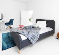A simple bedroom with a bed, a table, a chair, and a guitar in a 3-room apartment.