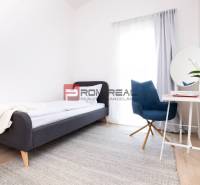 A bright room with a gray bed, a blue chair, and a table in a 3-room apartment.