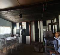 The interior of a cabin with a wooden ceiling, table, chairs, and a stove.