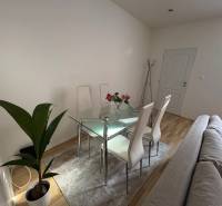 Glass dining table with four chairs in a 2-room apartment, next to a plant.