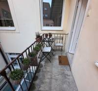 A narrow balcony with metal railings, chairs, and flower pots in a 2-room apartment.
