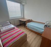 A room in a 3-room apartment with two beds, a table, and wooden flooring.