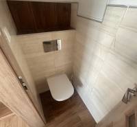 A toilet with light tiles and wooden details in a 3-room apartment.
