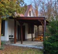 A cottage surrounded by greenery, with a wooden shelter, offers relaxation in nature.