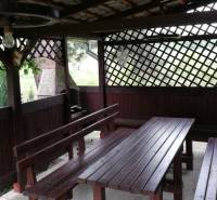 A wooden gazebo with benches located in the garden of a family house.