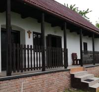 Family house with a terrace, wooden fence, and brick foundation in a natural setting.