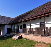 Family house with a porch, wooden beams, brick foundation, and a large grassy garden.
