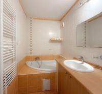 A bathroom in a 3-room apartment with a corner bathtub, sink, and radiator.
