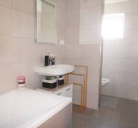 A bathroom in a family house with a bathtub, a sink, a shower corner, and large-format tiles.