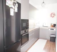 A kitchen in a family house with a black refrigerator and a built-in oven on a wooden floor.
