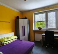 A room in a family house with a bed, a wardrobe, a desk, and yellow walls.
