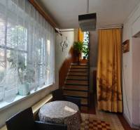 A hallway in a family house with a window, curtains, a table, chairs, and stairs with plants.