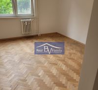 A room with wooden parquet and a radiator in a 3-room apartment with trees outside.