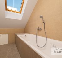 A bathroom in a family house with a bathtub under a skylight and beige tiles.