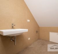 A sink in the attic bathroom of a family house with beige tiles and a sloped ceiling.