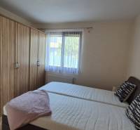 Bedroom in a family house with a bed, a large wardrobe, and a window with white curtains.