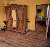 A room in a family house with a wooden wardrobe, a floor with a wooden decor, and light curtains.