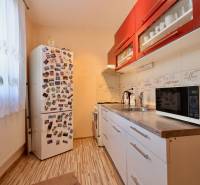 A kitchen in a studio apartment with red cabinets, a refrigerator, and a wooden decor floor.