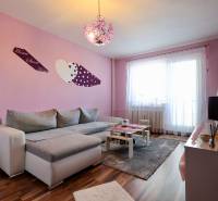 Living room in a studio apartment with pink walls and wood-patterned flooring.