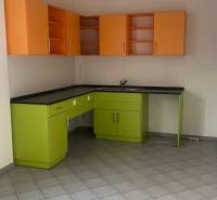 A kitchen unit with green and orange cabinets in an office on tiles.