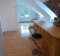 Two-room apartment with wood-patterned flooring, kitchen counter, and stools.