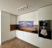 A kitchen in a 2-room apartment with a wooden decor floor, white cabinets, and built-in appliances.
