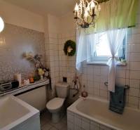 A bathroom in a 3-room apartment with a bathtub and a window, decorated with a curtain and flowers.