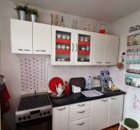 A kitchen in a 3-room apartment with white cabinets and decorative shelves.