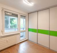 A room with a wooden decor floor, a built-in wardrobe, and balcony doors in a 3-room apartment.
