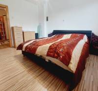 A bedroom in a family house with a double bed, a wooden-patterned floor, and a dresser.