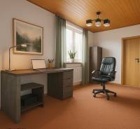 The interior of a study in a family house with a wooden ceiling, green curtains, and a black chair.