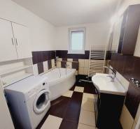 Bathroom in a family house with a washing machine, corner bathtub, and sink.