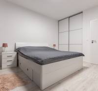 A bedroom with white furniture, a double bed, and a floor with a wood decor in a two-room apartment.