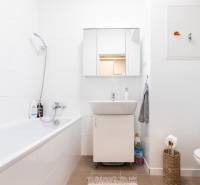 Bathroom in a 2-room apartment with a bathtub, sink, and toilet, white tiles combined with a brown floor.
