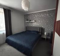 A bedroom with dark bedding, gray walls, and a designer lamp in a two-room apartment.