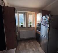 Kitchen in a 2-room apartment with three windows, tiles, and kitchen cabinets.