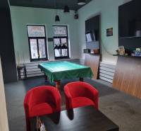 Commercial space with a pool table, red armchairs, and a table with games.