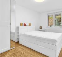 Bright bedroom with white furniture, bed, and wood-decorated flooring in a family house.