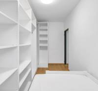White room in a family house with a bed, shelves, and a wooden-patterned floor.