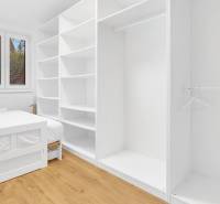 A bright bedroom in a family house with a white bed, a large wardrobe, and a wooden-patterned floor.