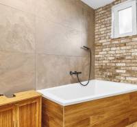 A bathroom in a family house with a bathtub, a brick wall, and a wooden decor floor.