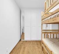 A room in a family house with a bunk bed, a white wardrobe, and a wooden-patterned floor.