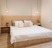A bedroom with light furniture, pendant lights, and a wood-patterned floor.