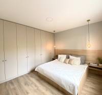 A bedroom in a 4-room apartment with a white bed, wardrobes, and a floor with a wooden decor.
